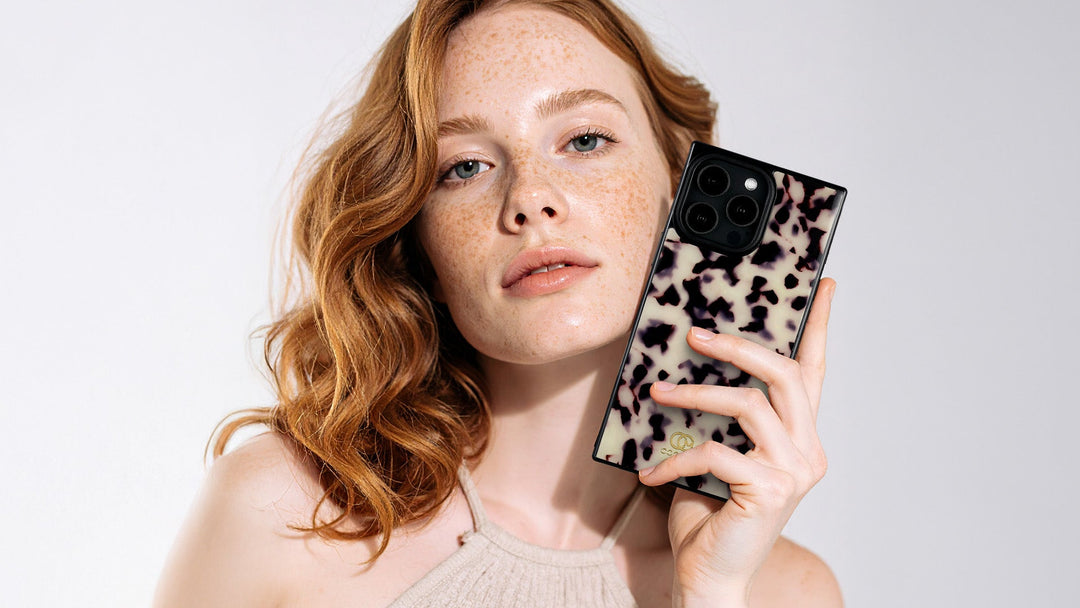 Redheaded woman holds a cream and black tortoiseshell phone case beside her face