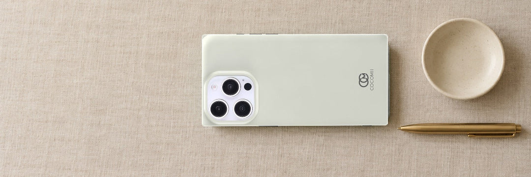 COCOMII Solid rectangle case lying sideways on pale oatmeal linen beside a brass pen