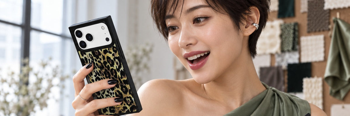 Woman in a sage green top at a standing desk in a loft studio reading a message with a COCOMII leopard print case in Ivory