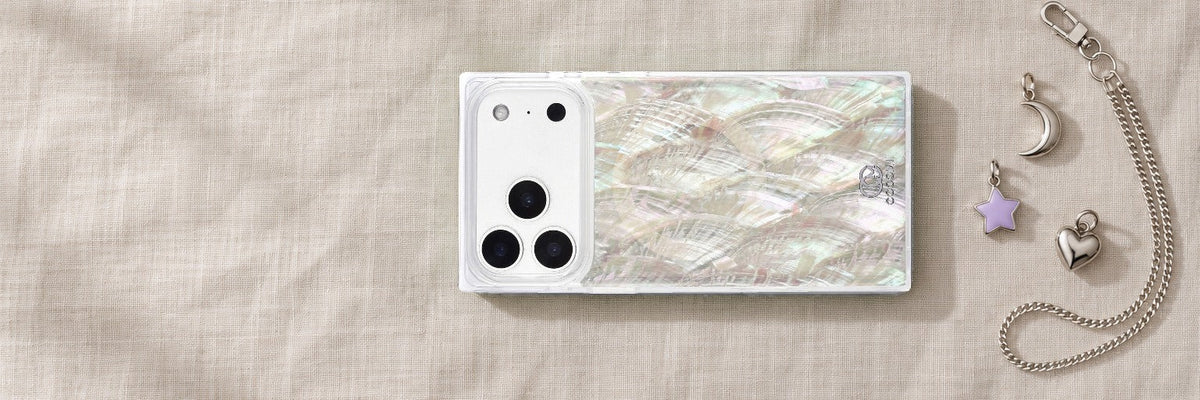 COCOMII Real Mother of Pearl rectangle case on oatmeal linen beside silver moon, star and heart charms and a silver chain