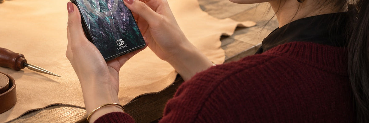 Woman in an oxblood knit at a leather workshop bench checking the finish with a COCOMII Mother of Pearl case in Black