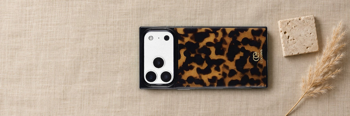 COCOMII Tortoiseshell rectangle case lying on warm oat linen beside a travertine tile and a dried pampas stem