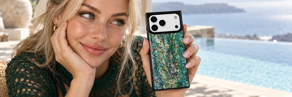 Woman in an emerald crochet-knit top on a resort pool terrace holding a COCOMII abalone finish case in Aurora