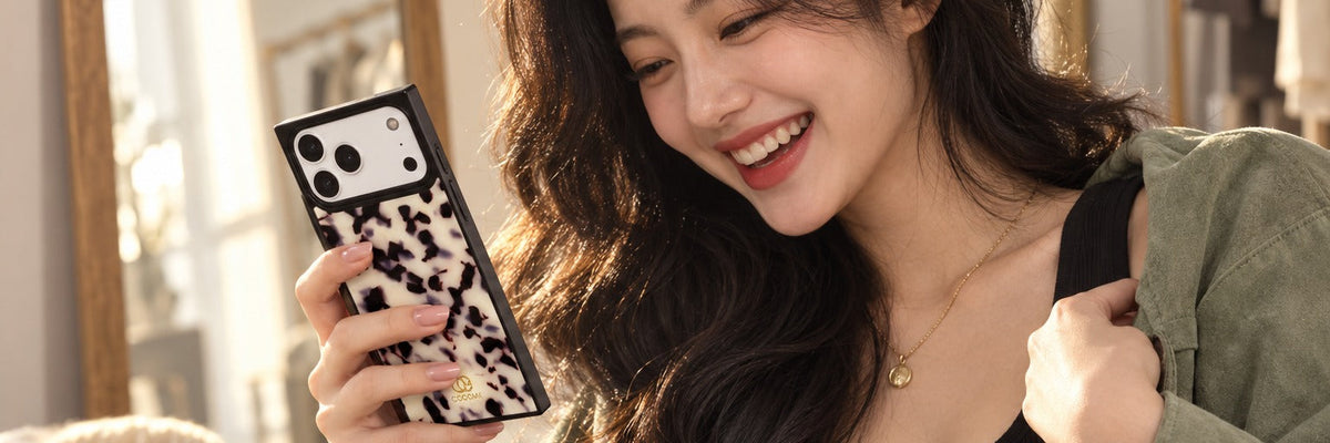 Woman in a sage suede overshirt in an atelier laughing at a message with a COCOMII tortoiseshell pattern case in Ivory