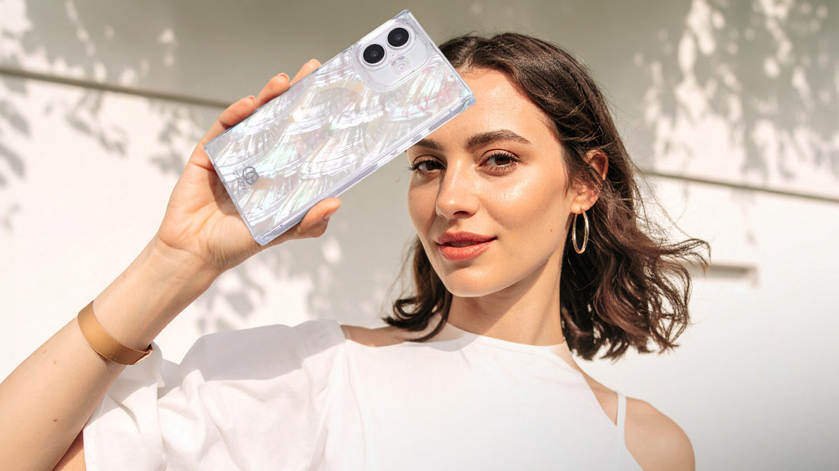 Woman in a white top holding an iridescent COCOMII rectangle iPhone case up in the sunlight